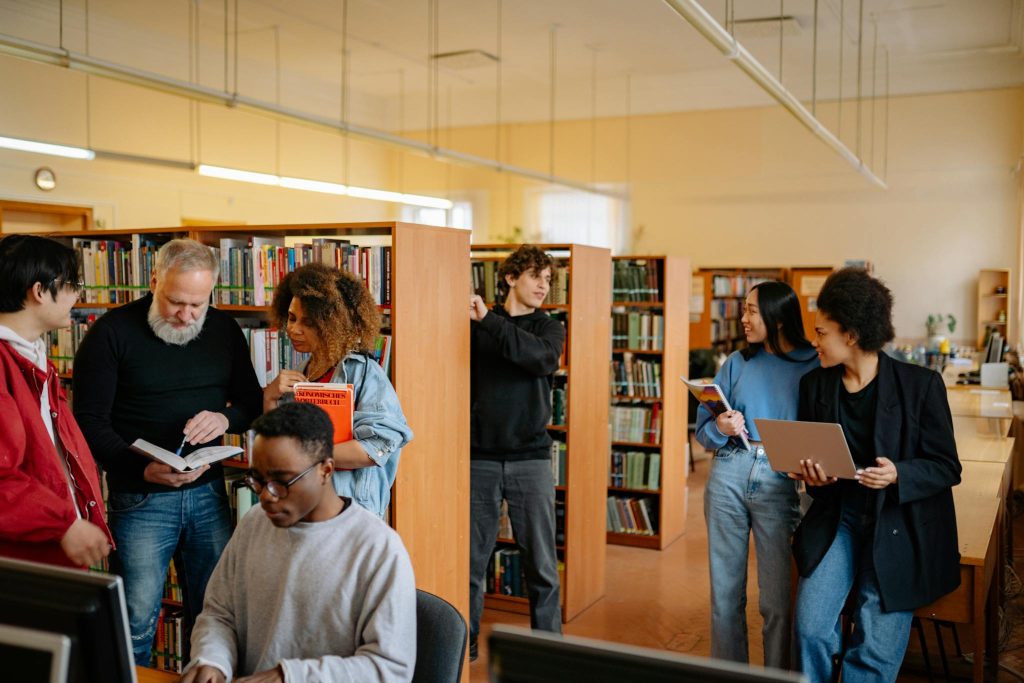 A diverse group of students engage in study activities in a bright library setting.