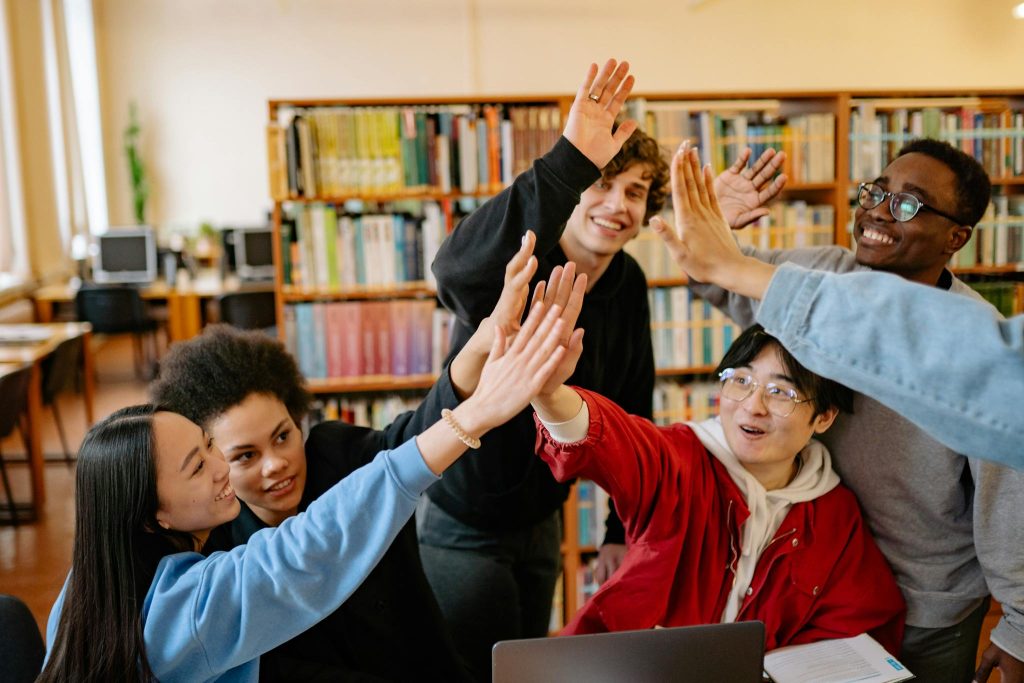 Group of happy students high-fiving in a library setting, celebrating success.