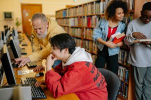 Students collaborating and learning in a library setting, engaging with computers and books.