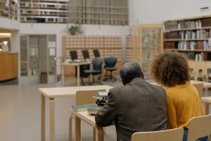 Two people studying together in a cozy modern library setting filled with bookshelves and study tables.