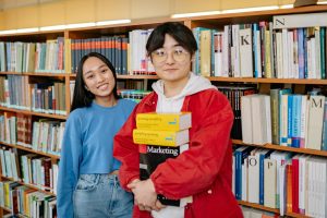Two students smiling in a library holding books. Ideal for education themes.
